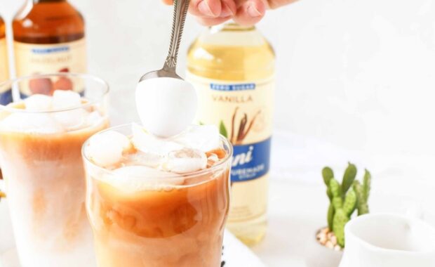 hand holding spoon pouring milk foam on top of iced tea