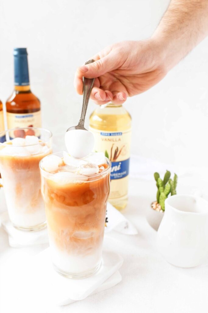 hand holding spoon pouring milk foam on top of iced tea