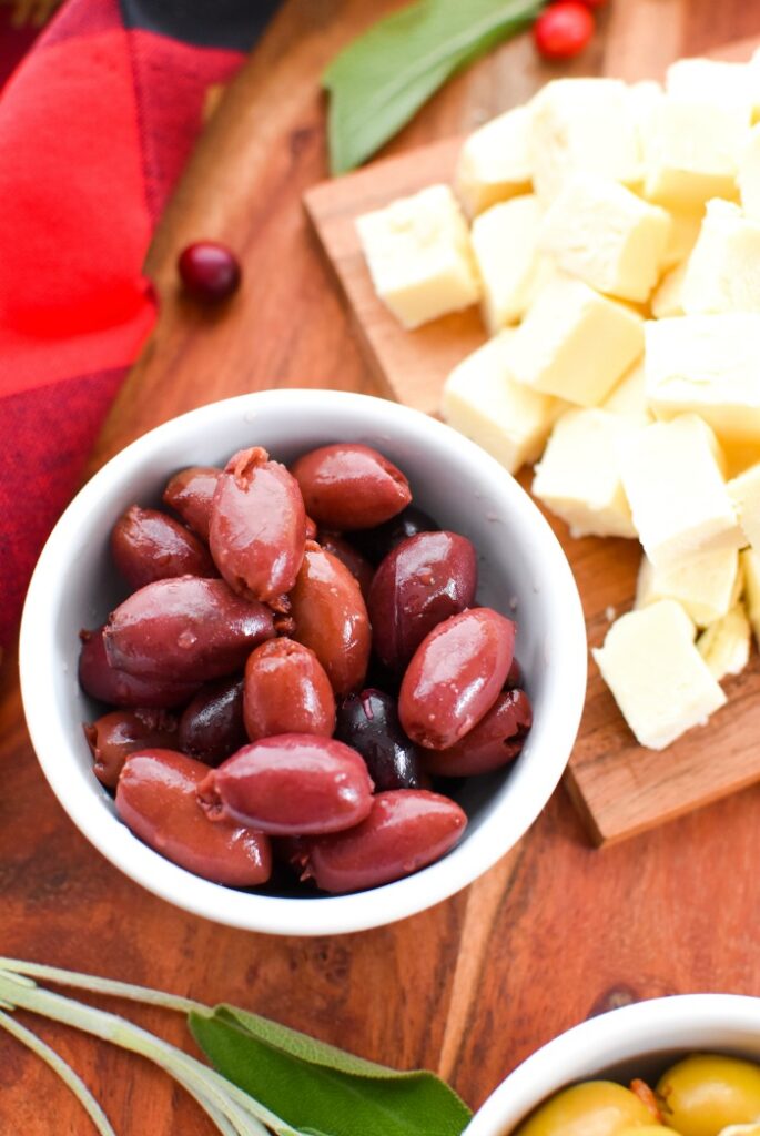 small white bowl of olives, cubed cheese on wood