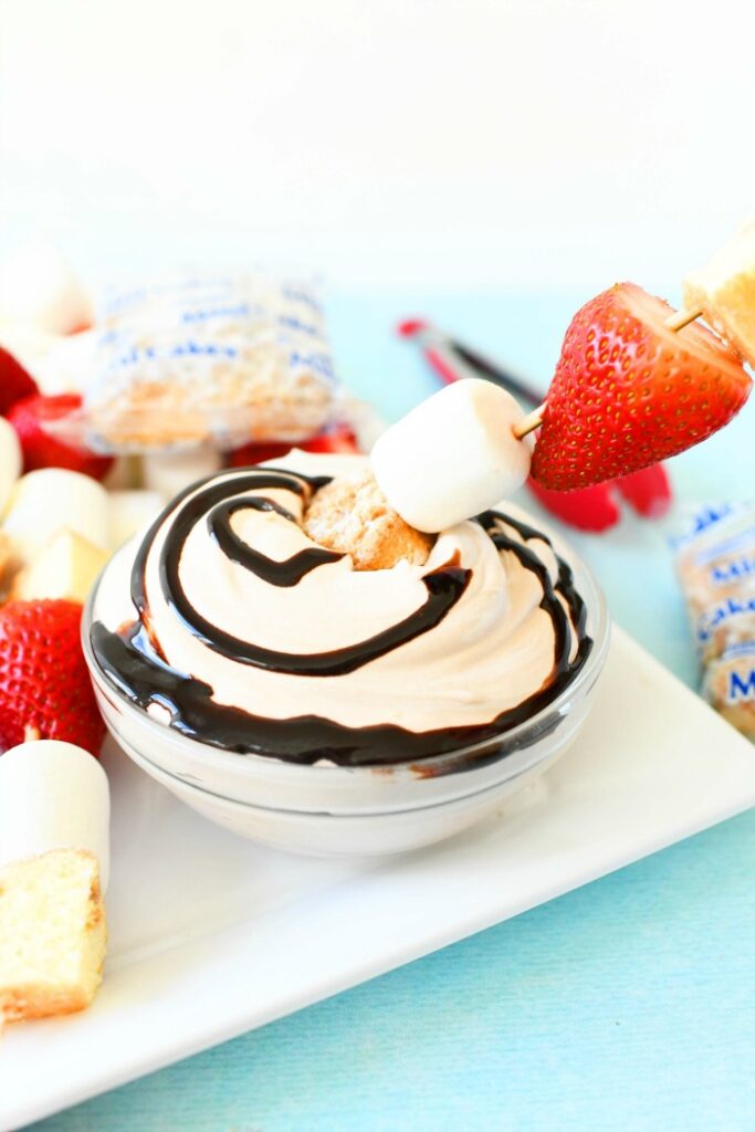 cake, marshmallow, strawberry on kabob dipped into whipped cream. chocolate syrup swirled on top