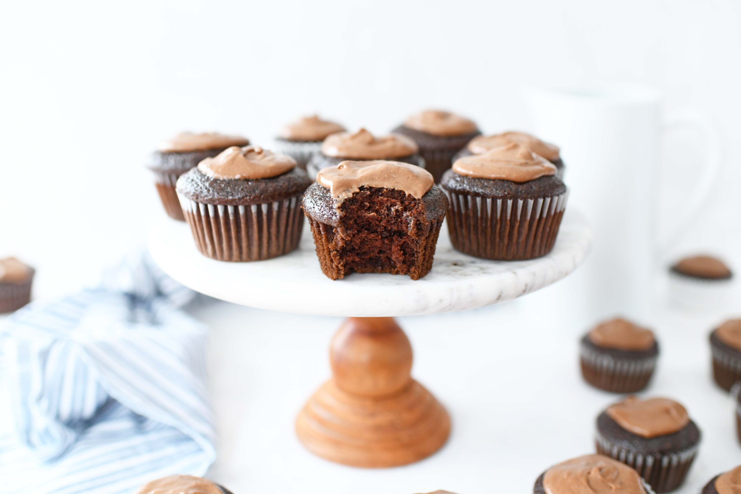 Chocolate Mayo Cupcakes with Mayo Ganache on a marble cake stand with a blue striped napkin nearby.