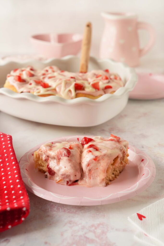 Strawberry cinnamon buns on a pink plate with strawberry cinnamon rolls in the background.