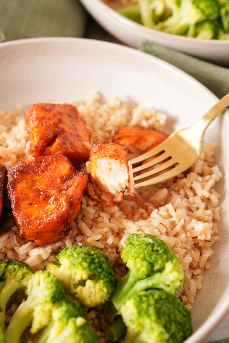 A gold fork with a piece of salmon on it near broccoli and rice.