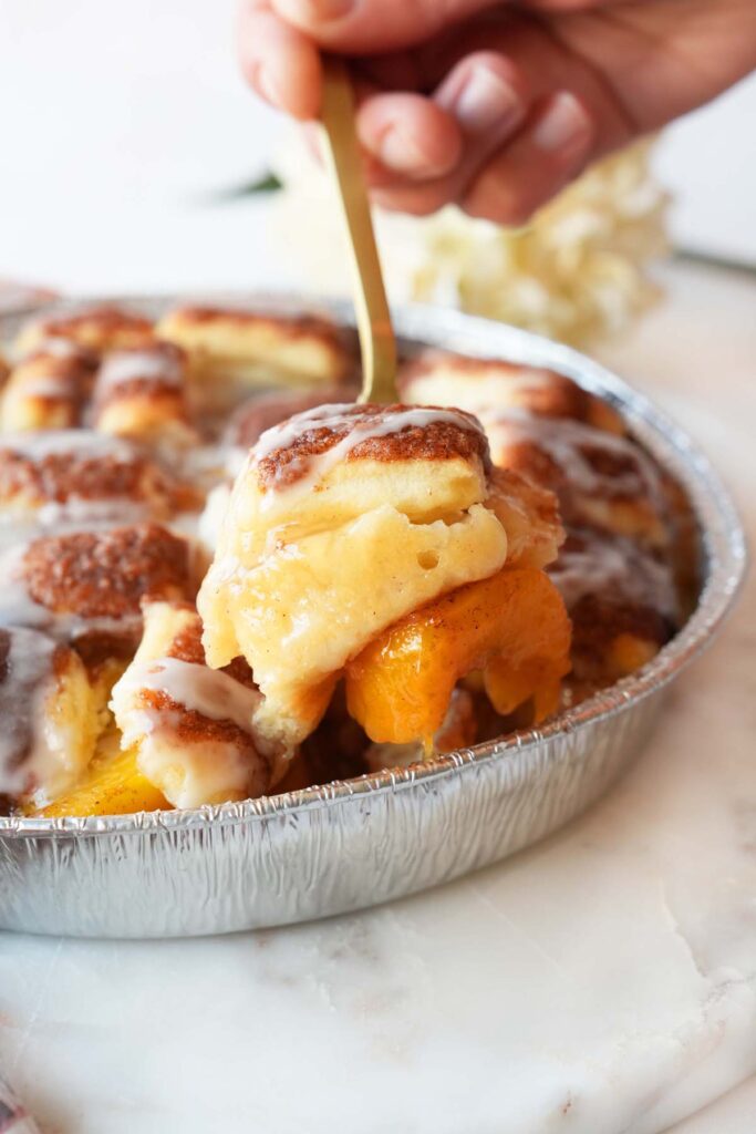 A gold fork with peach bun cobbler on it.