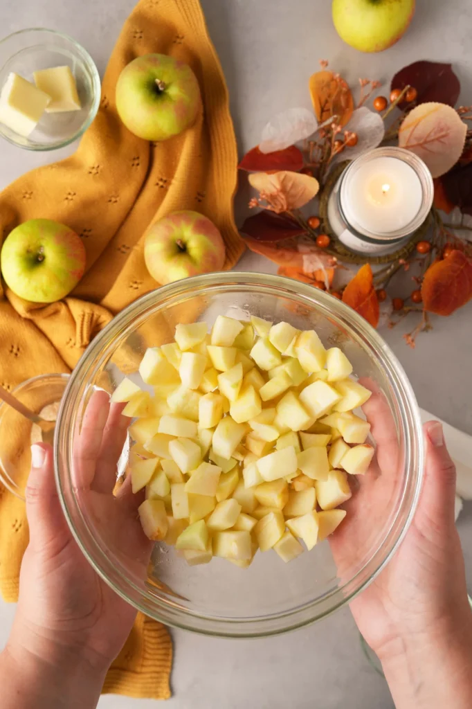 Bowl of diced apples held above an autumn baking setup.