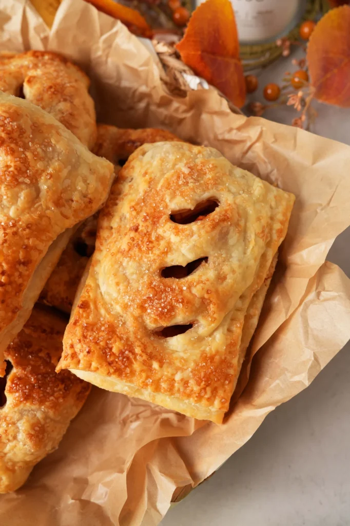 Finished apple hand pies stacked in parchment paper with autumn styling.