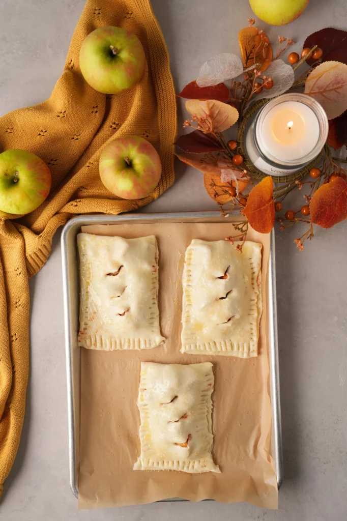 Unbaked apple hand pies on a parchment-lined baking sheet.
