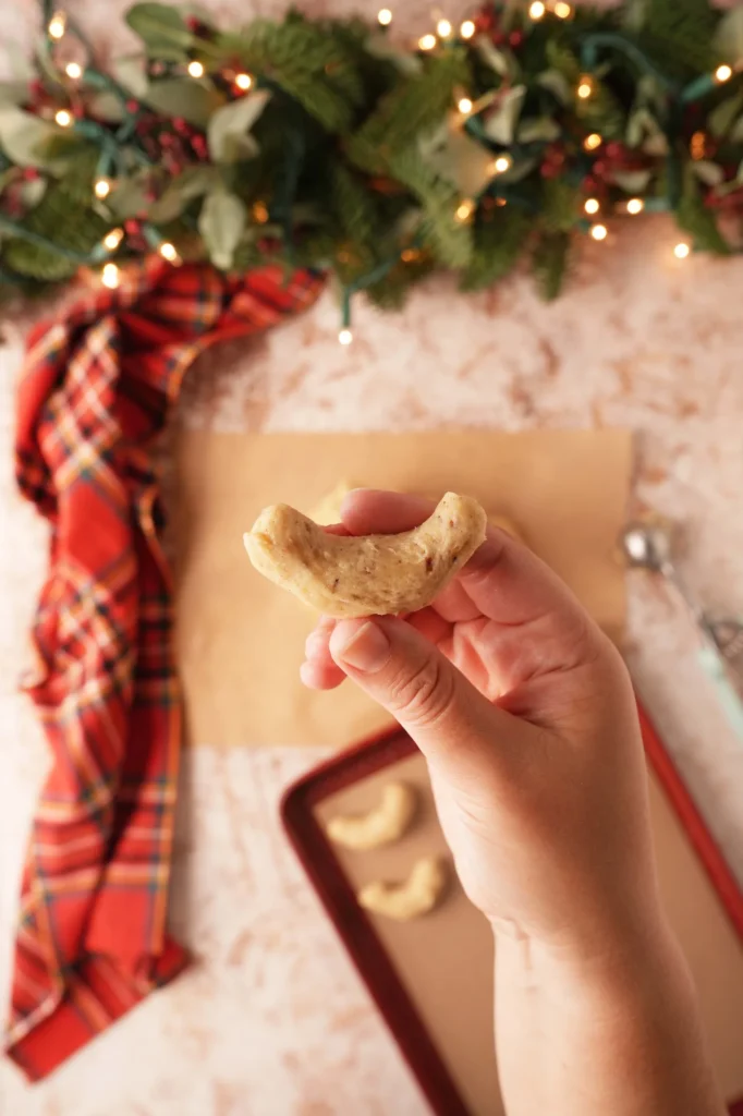 Hand holding a shaped crescent cookie before baking.