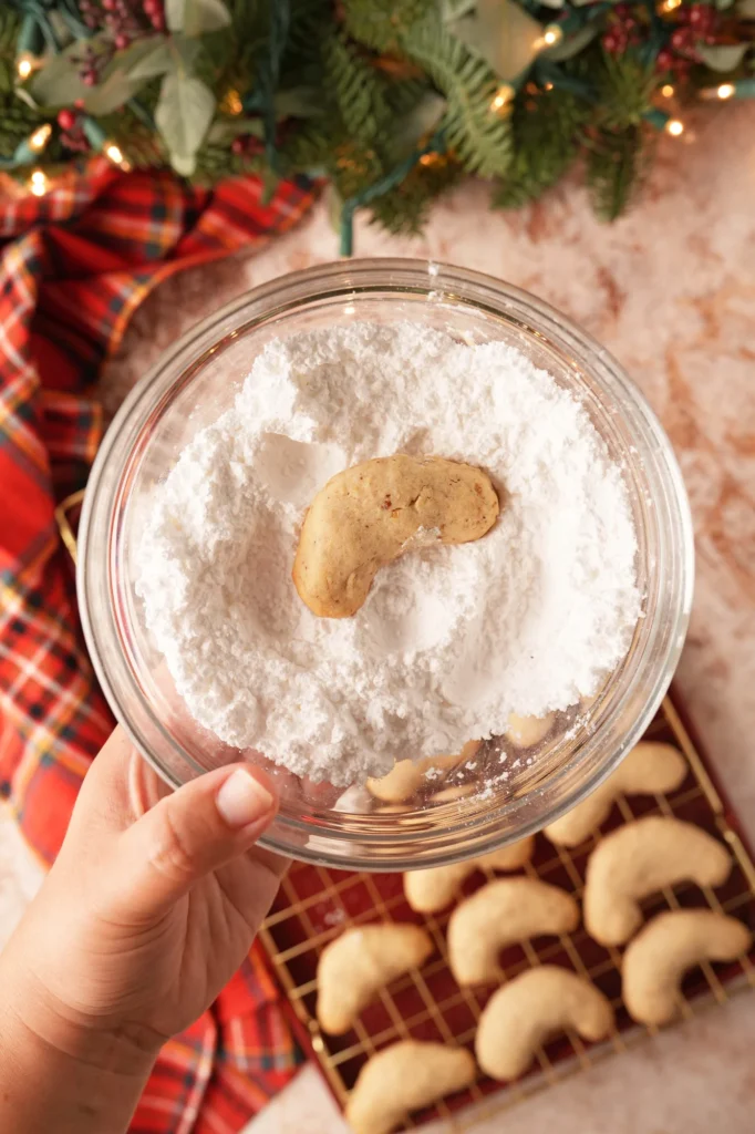 Warm crescent cookie being coated in powdered sugar.