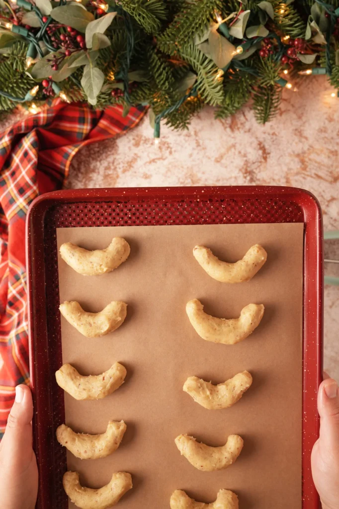 Unbaked crescent-shaped cookie dough on a parchment-lined baking sheet.
