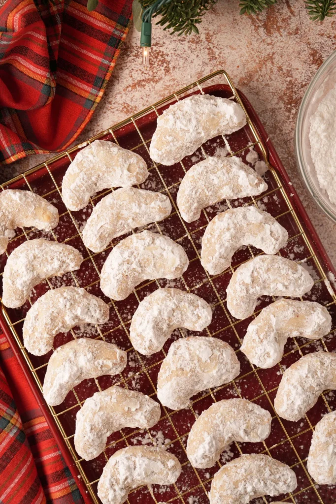 Powdered crescent cookies cooling on a wire rack with holiday styling.