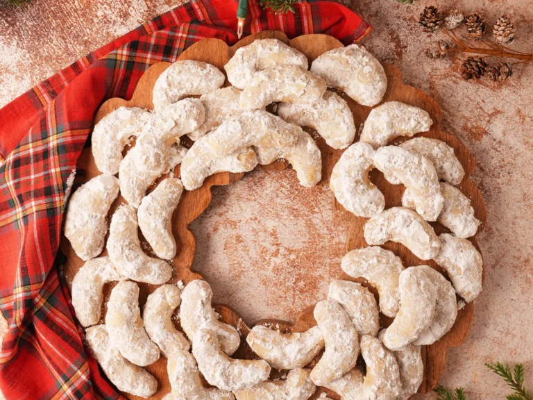Swedish heirloom crescent cookies arranged in a holiday wreath with evergreen branches and tartan fabric.